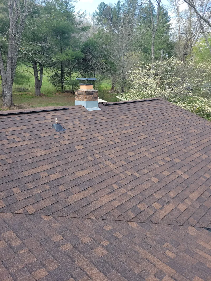 Brown shingle roof with a chimney, looking out over wooded hills