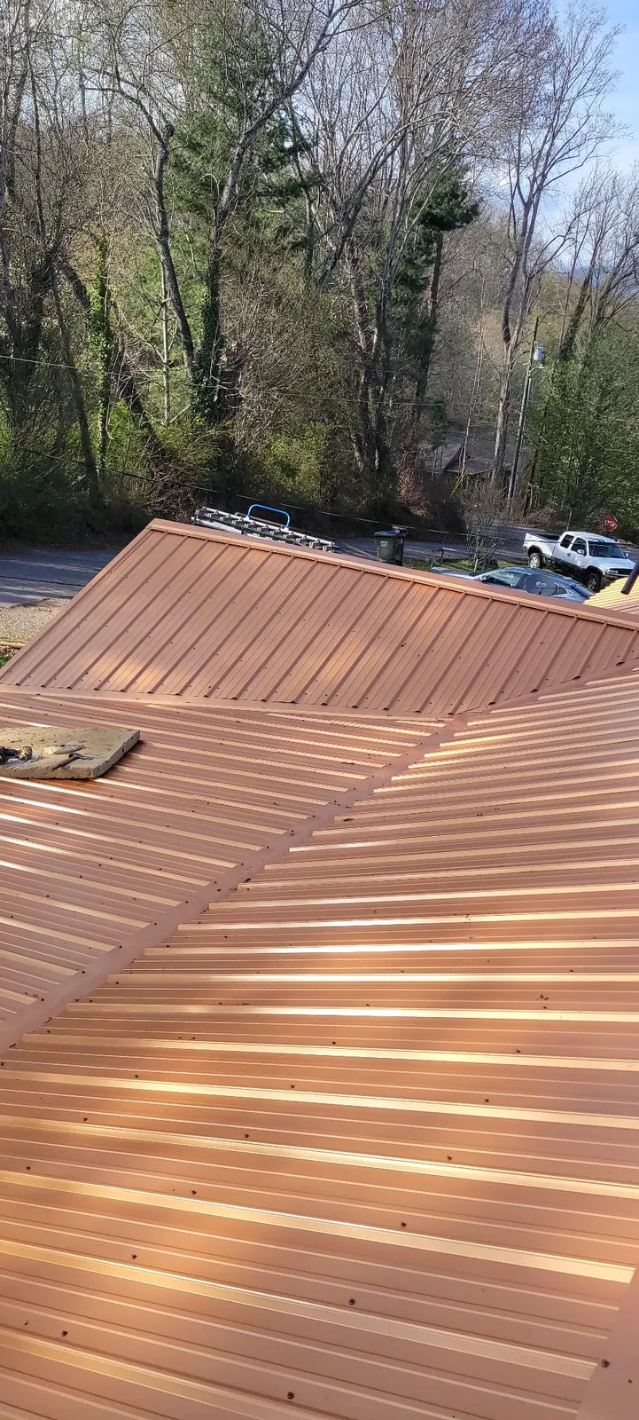 Copper-tone standing-seam metal roof panels, freshly installed, with trees behind