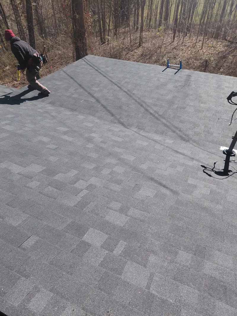 Crew working on a low-slope roof section with gray underlayment laid, trees behind