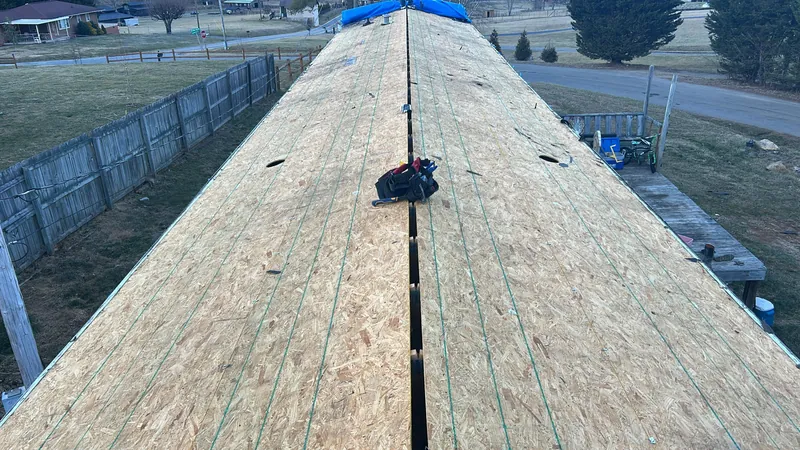 New OSB roof decking on a house before underlayment, looking along the ridge toward a fenced yard