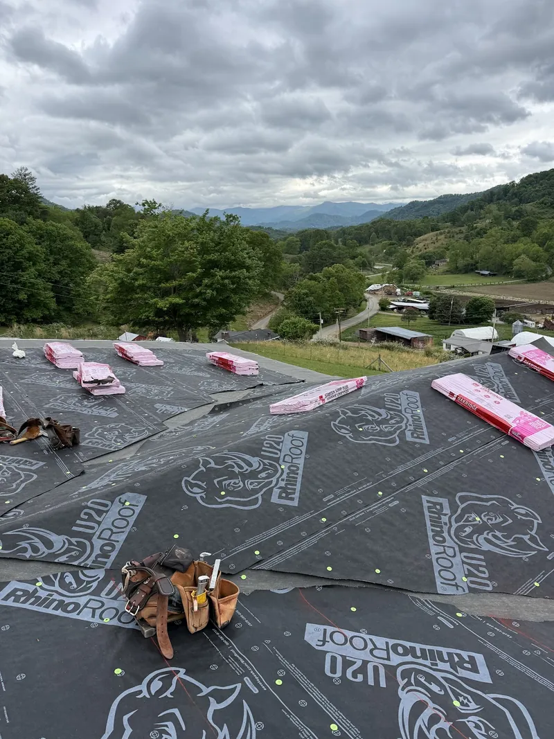 Synthetic underlayment laid across a roof deck, with wooded mountain ridgelines behind under an overcast sky