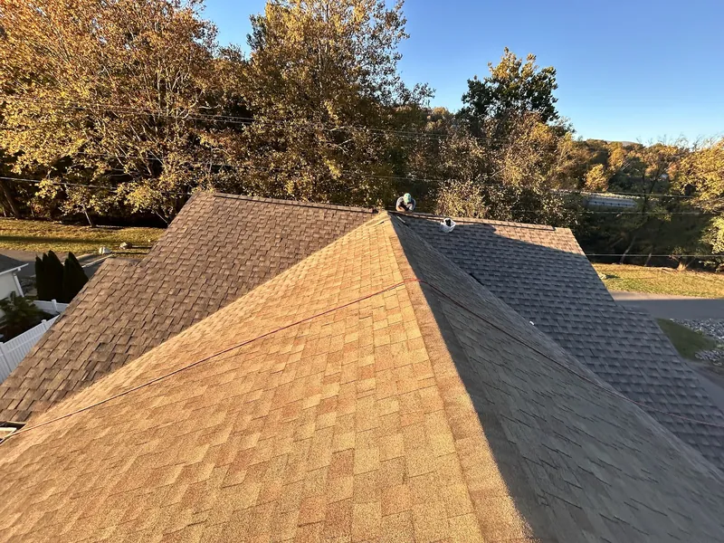 Arolite Group crew members on a new brown architectural shingle roof, with fall color in the trees behind the house