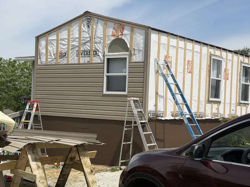 Vinyl siding going up over house wrap on a two-story home, with ladders against the wall and siding stacked on sawhorses